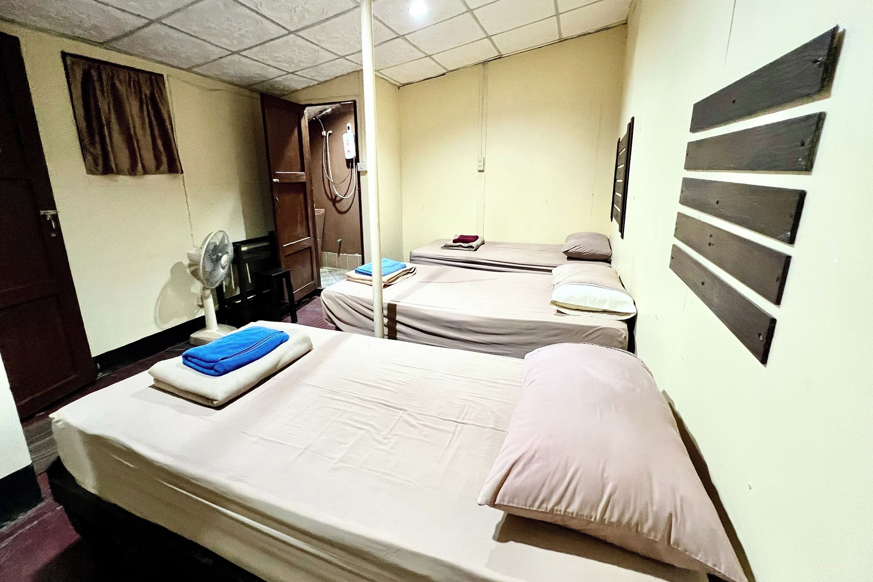 A room with two beds, a wooden wardrobe, a fan, and a shower.