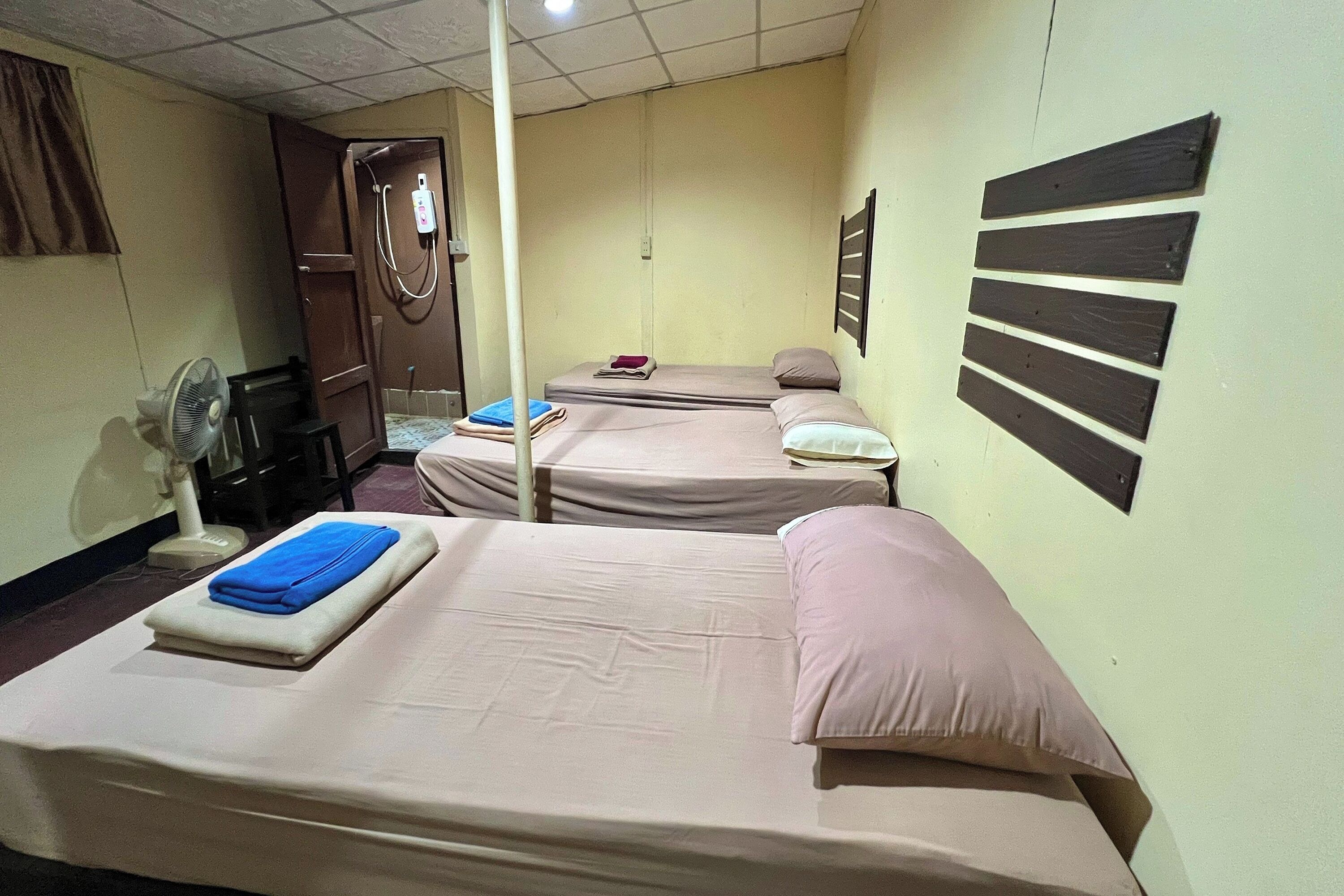 A room with two beds, a fan, a wardrobe, and a wall-mounted shelf.