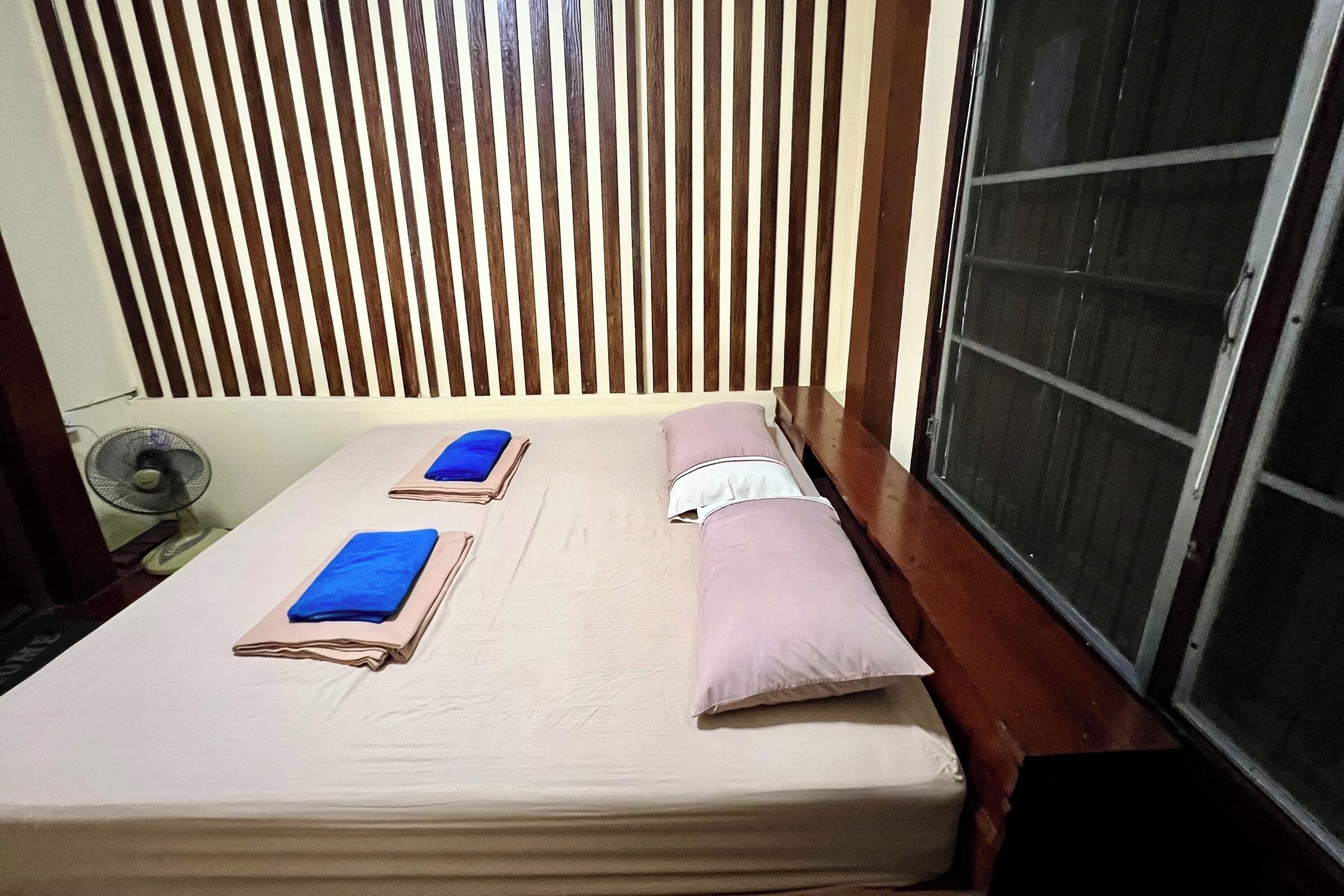 A single bed with a beige mattress, two pillows, and a blue towel.