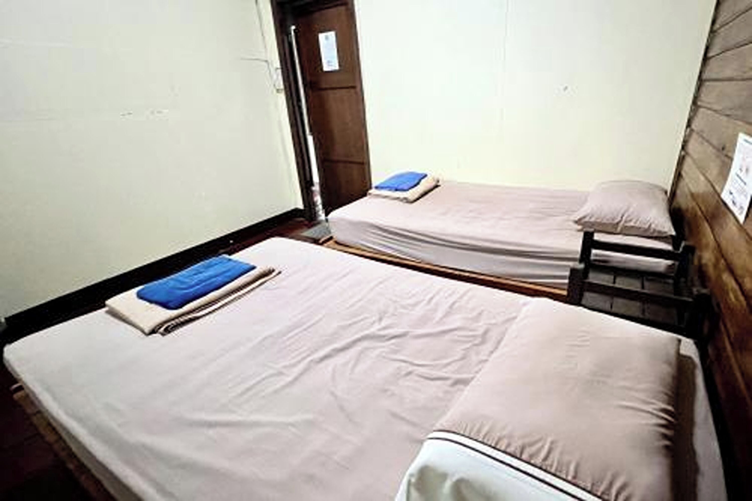 Deux lits simples avec du linge de lit blanc et des serviettes bleues, une porte en bois et un mur blanc.