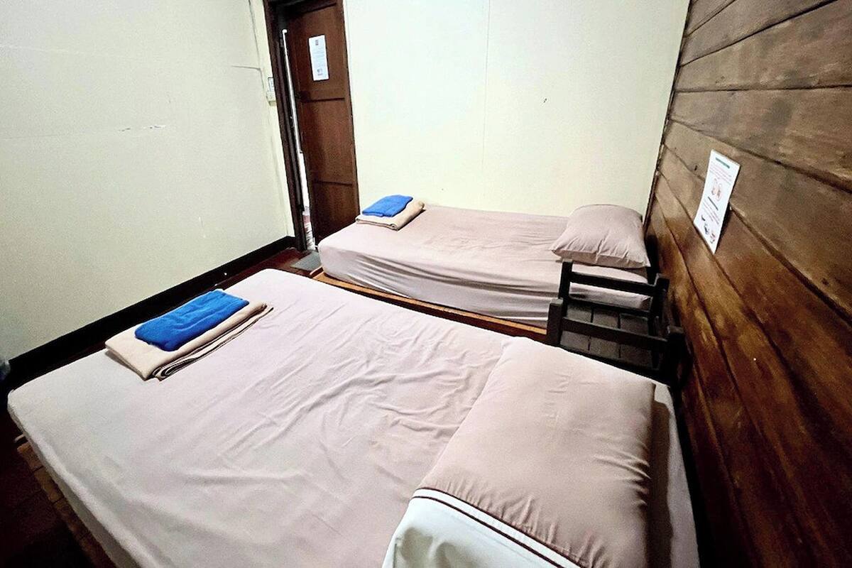 Two single beds with white linens and blue towels, wooden walls, and a door in the background.