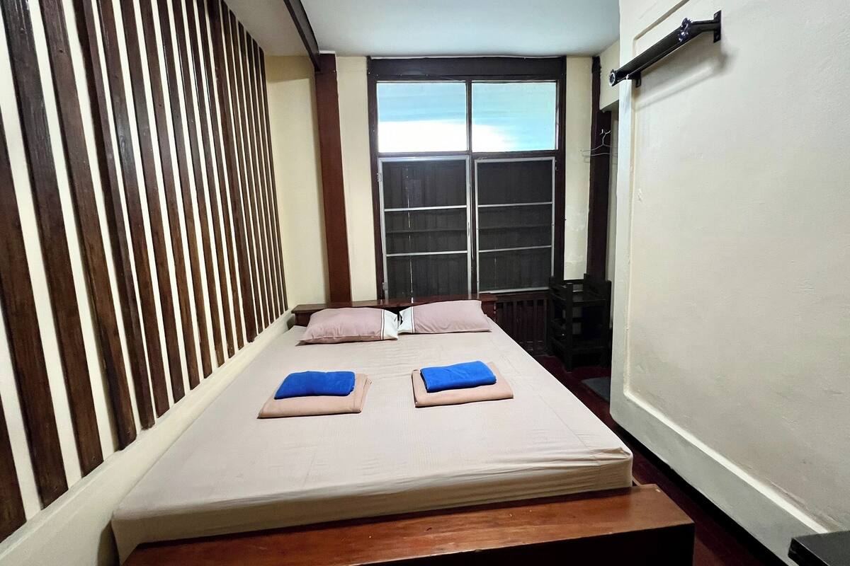 A single bed with a wooden headboard, a window with a view, and a small bedside table.