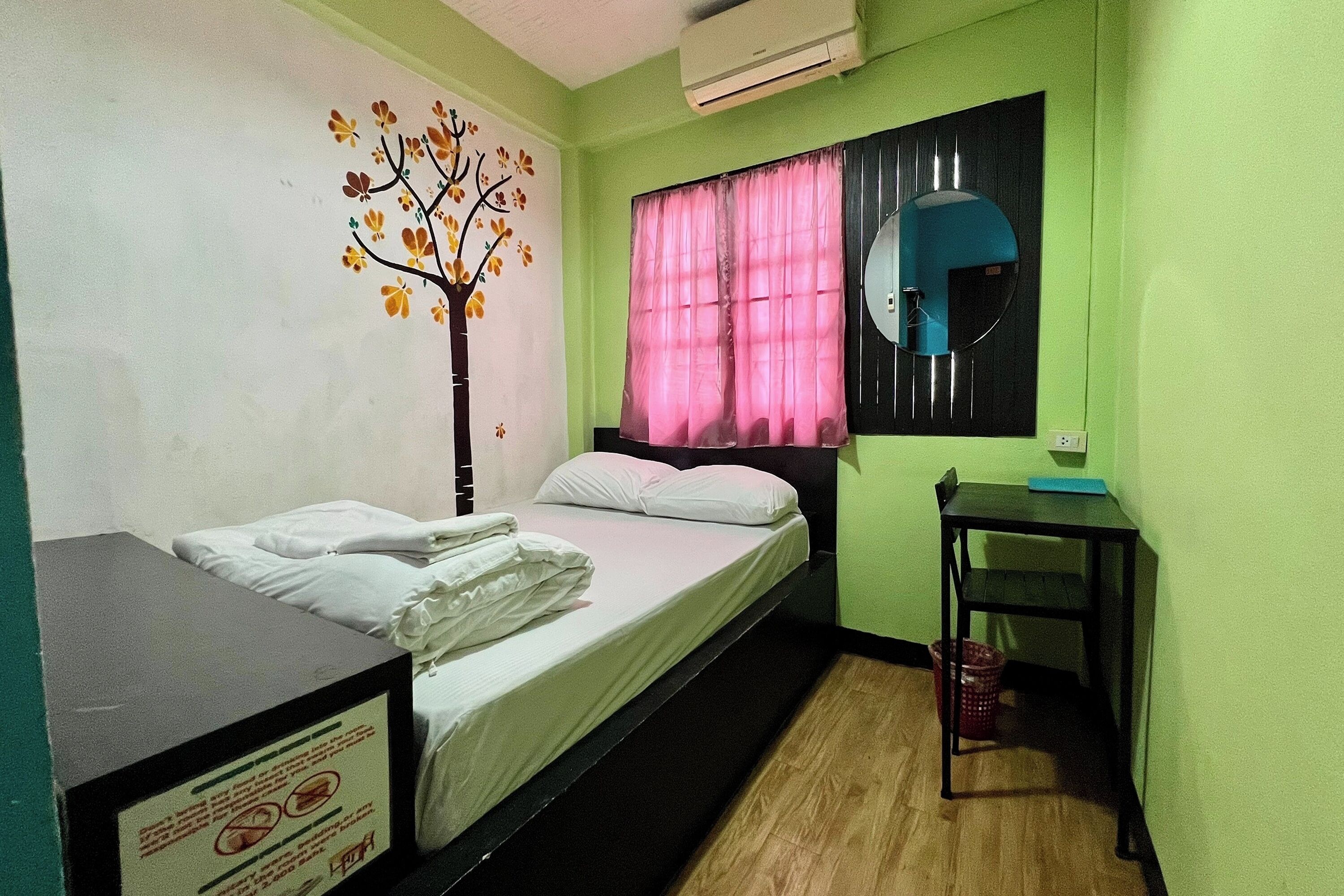 Una habitación con cama, escritorio, espejo y decoración en la pared.