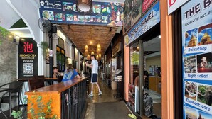 A corridor with a bar on the left, a travel agency on the right, and a restaurant named 'Shong Cha' with a QR code. - Baan Lanna At Phrasingh (Chiang Mai)