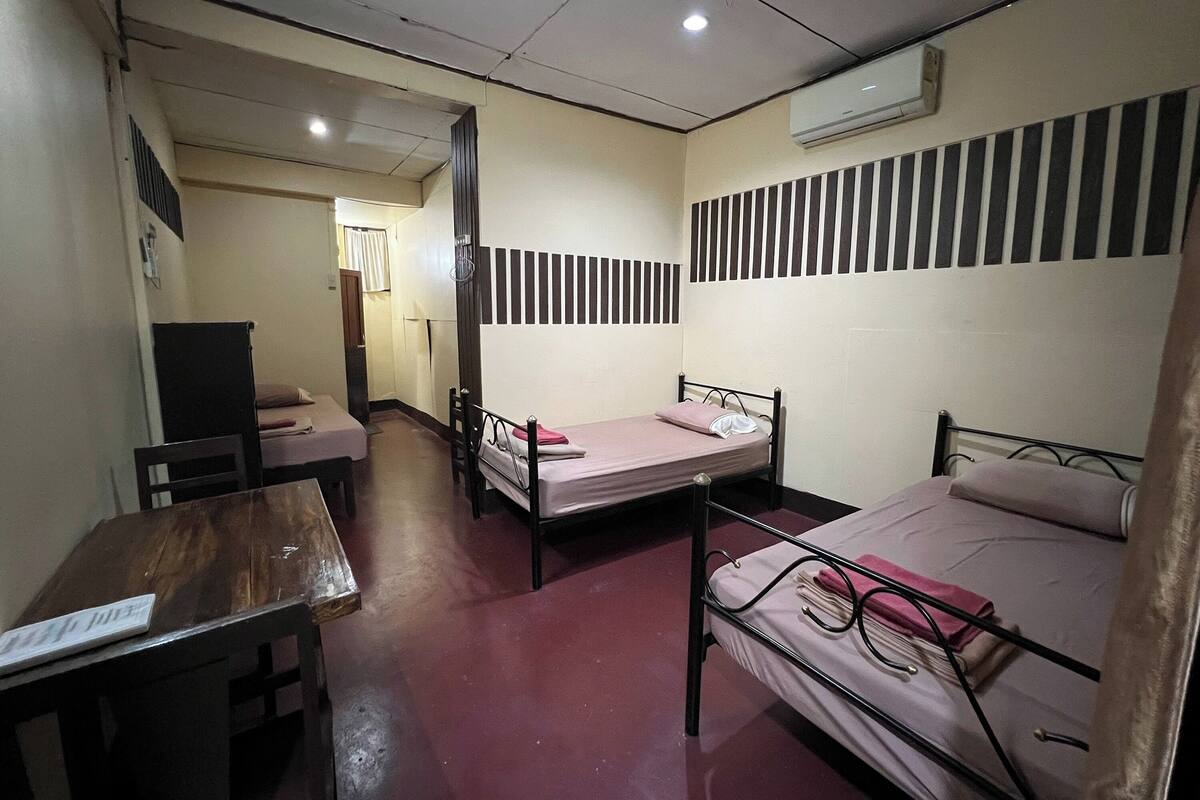 A dormitory room with two beds, a wooden table, and a desk.