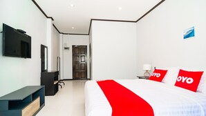 Quarto de hotel com cama, televisão presa na parede, escrivaninha e porta que dá para outro cômodo.