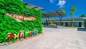 Entrada de hotel com galeria coberta, placa de sinalização e sebe verde exuberante.