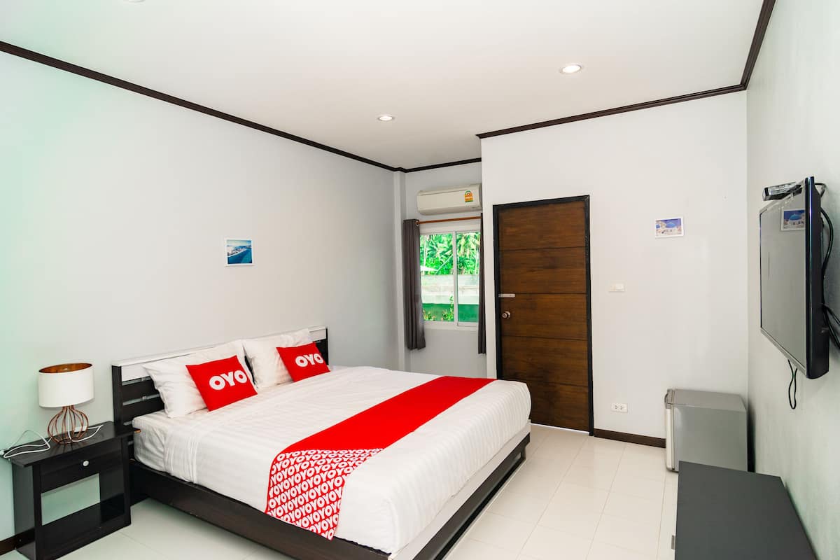 A hotel room with a bed, a nightstand, a lamp, a TV, and a door.