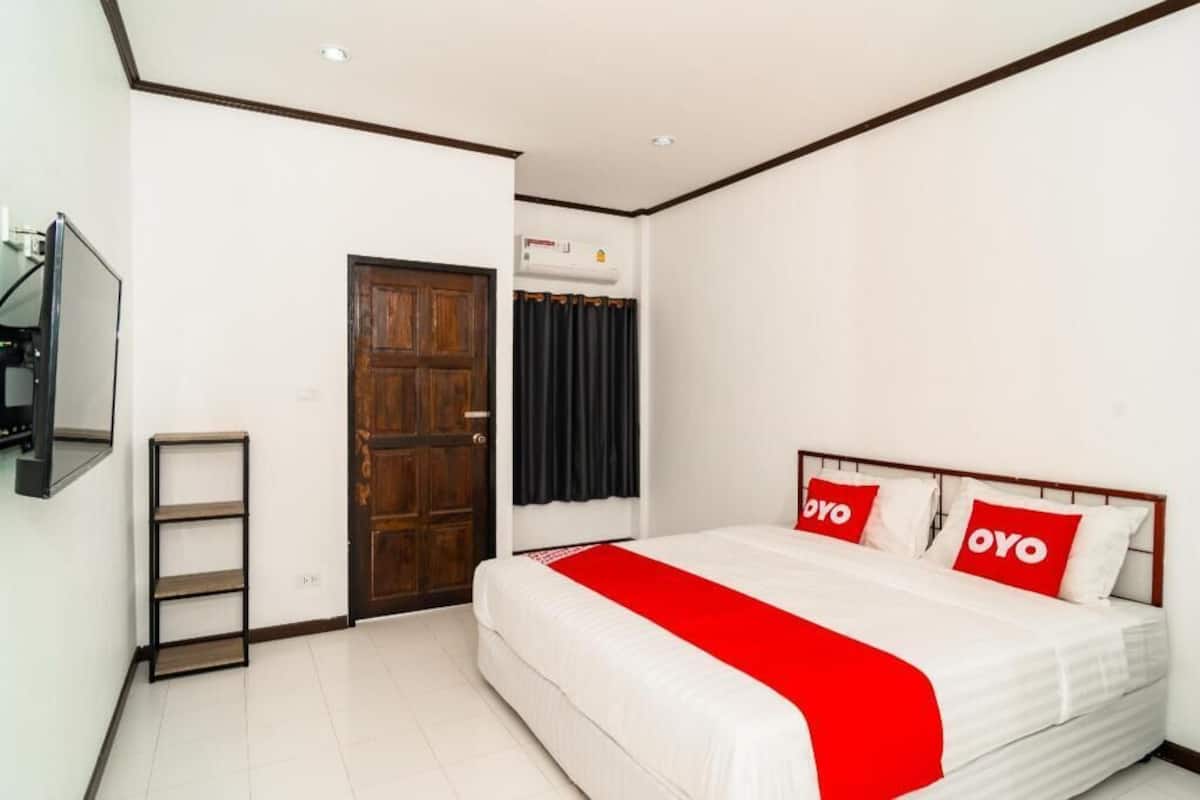A hotel room with a bed, a TV, a wooden door, and a window with curtains.