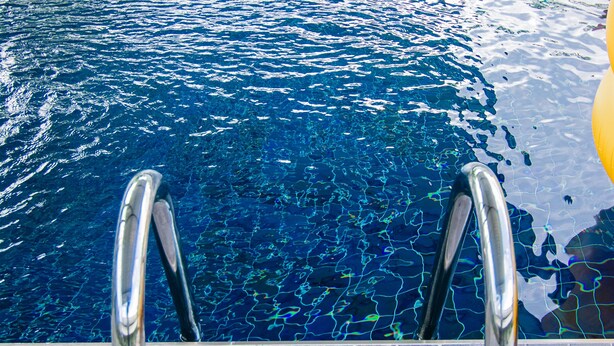 Piscina com água azul cristalina e escadas de metal.