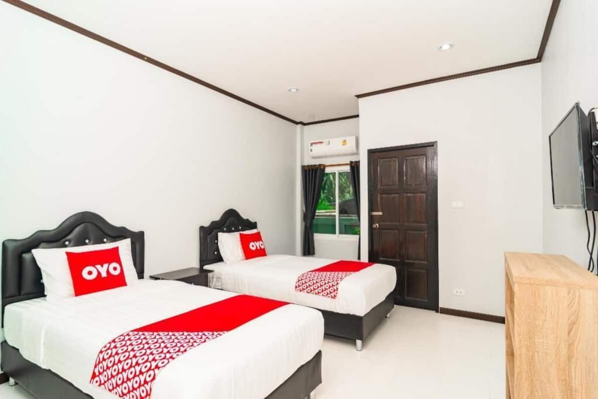 A hotel room with two beds, a TV, an air conditioning unit, and a wooden side table.