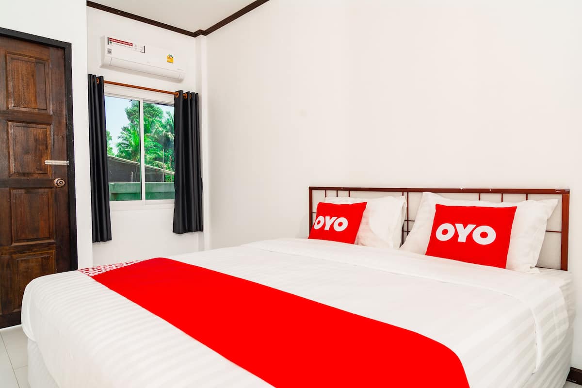 A hotel room with a bed, two pillows with the word "OYO" on them, a red blanket, a wooden door, and an air conditioning unit.