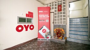 A hallway with a large OYO Hotels advertisement, a window, and a door with a decorative shrine. - OYO 525 MRT Phetkasem 48 Place (Bangkok)