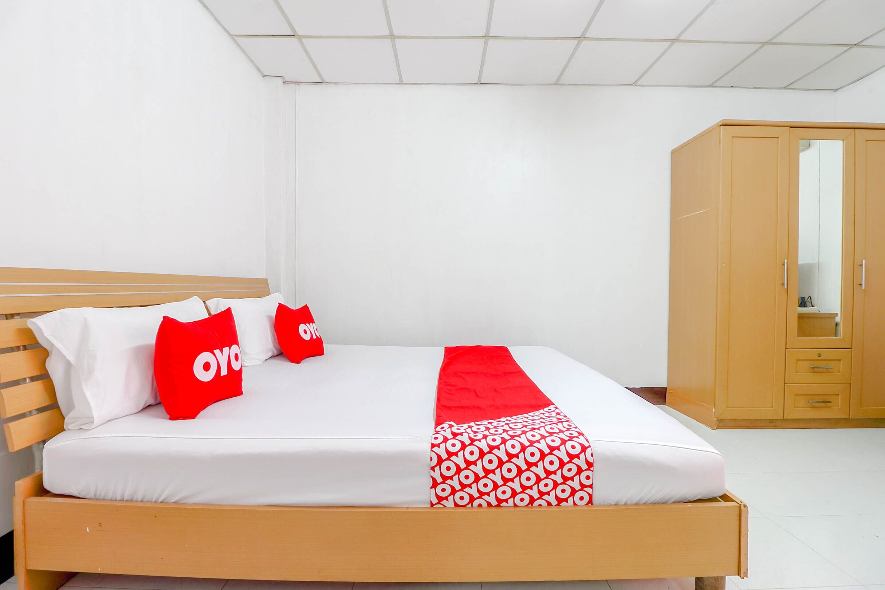 A neatly made bed with white and red bedding, a wooden headboard, and a wardrobe with a mirror.
