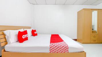 A neatly made bed with white and red bedding, a wooden headboard, and a wardrobe with a mirror.