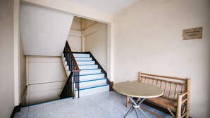 A staircase with blue steps, a wooden bench, and a small table in a room with plain walls. - OYO 525 MRT Phetkasem 48 Place (Bangkok)