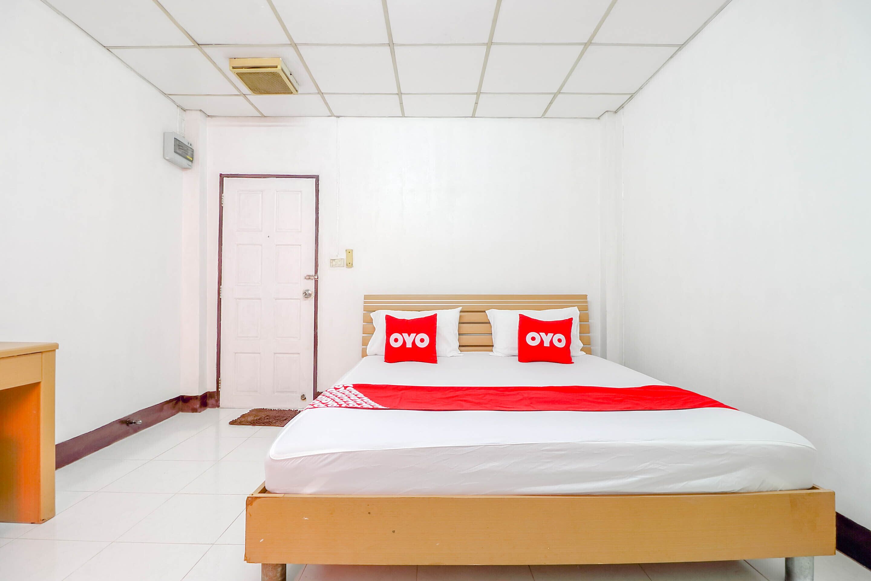 A hotel room with a bed, a wooden headboard, a red and white bedspread, and a white door.