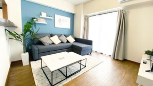A modern living room with a grey sofa, a white coffee table, and a blue accent wall. - OUCHI HOTEL Dambara (Hiroshima)
