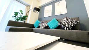 A modern living room with a grey sofa, patterned cushions, and abstract wall art. - OUCHI HOTEL Dambara (Hiroshima)