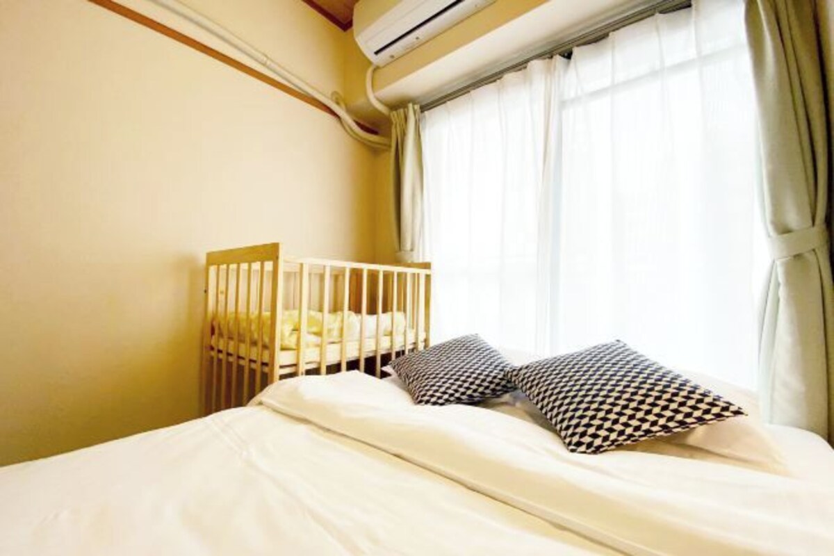 A bedroom with a crib, white bedding, and patterned pillows.