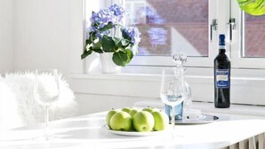 Una cocina moderna con encimera blanca, ventana con vistas, una botella de licor y un florero con flores.