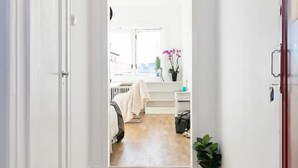 Un pasillo con piso de madera que conduce a una habitación con cama, ventana y una planta.