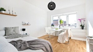 Un dormitorio moderno con cama, escritorio y silla. Se ve una ventana con vistas a edificios.