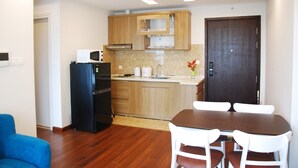 Una cocina compacta con muebles de madera, un refrigerador negro y una mesa de comedor con sillas blancas.