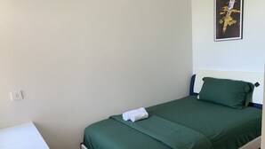 Una cama individual con ropa de cama verde, una mesita de noche blanca y una lámpara de pared.