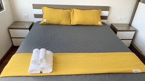 Una cama bien hecha con cubrecama gris y amarillo, dos almohadas amarillas y un par de toallas blancas sobre un detalle decorativo amarillo.