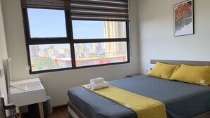 Una cama bien hecha con vistas a la ciudad, un escritorio pequeño y una ventana con persianas.