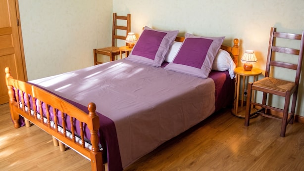A neatly made bed with a wooden frame and a purple bedspread, flanked by two wooden nightstands with lamps, in a room with wooden flooring and a plain wall. - Homerez - House in La Couarde-sur-Mer (La Couarde-sur-Mer)