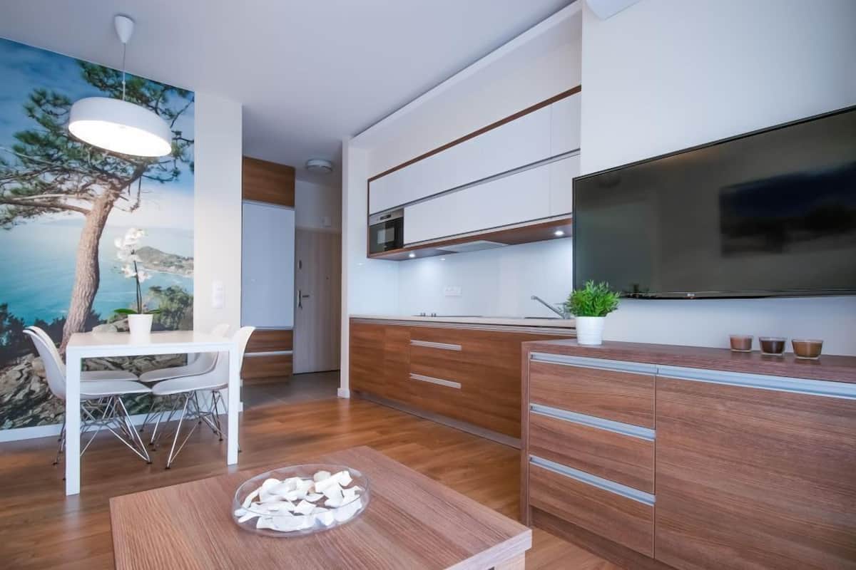A modern kitchen with wooden cabinets, a dining table, and a TV mounted on the wall.