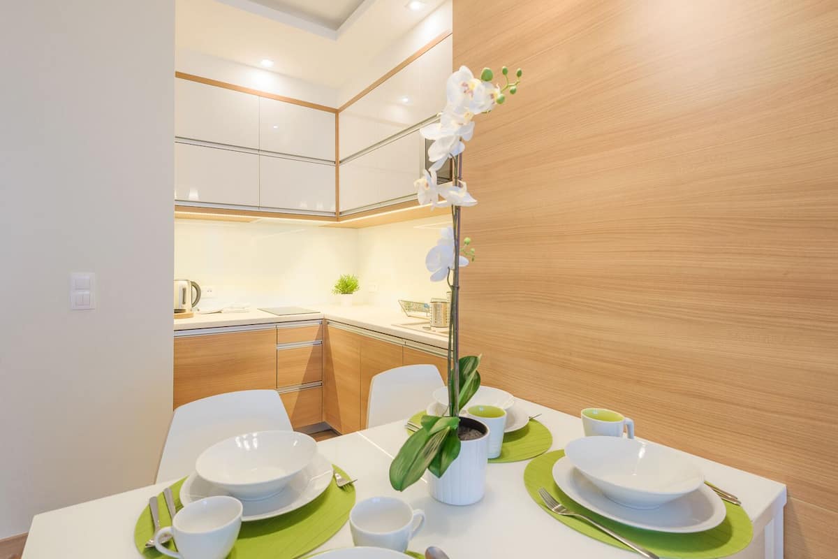 A modern kitchen with white cabinets, a countertop, and a dining area set with white plates, green placemats, and a potted orchid.