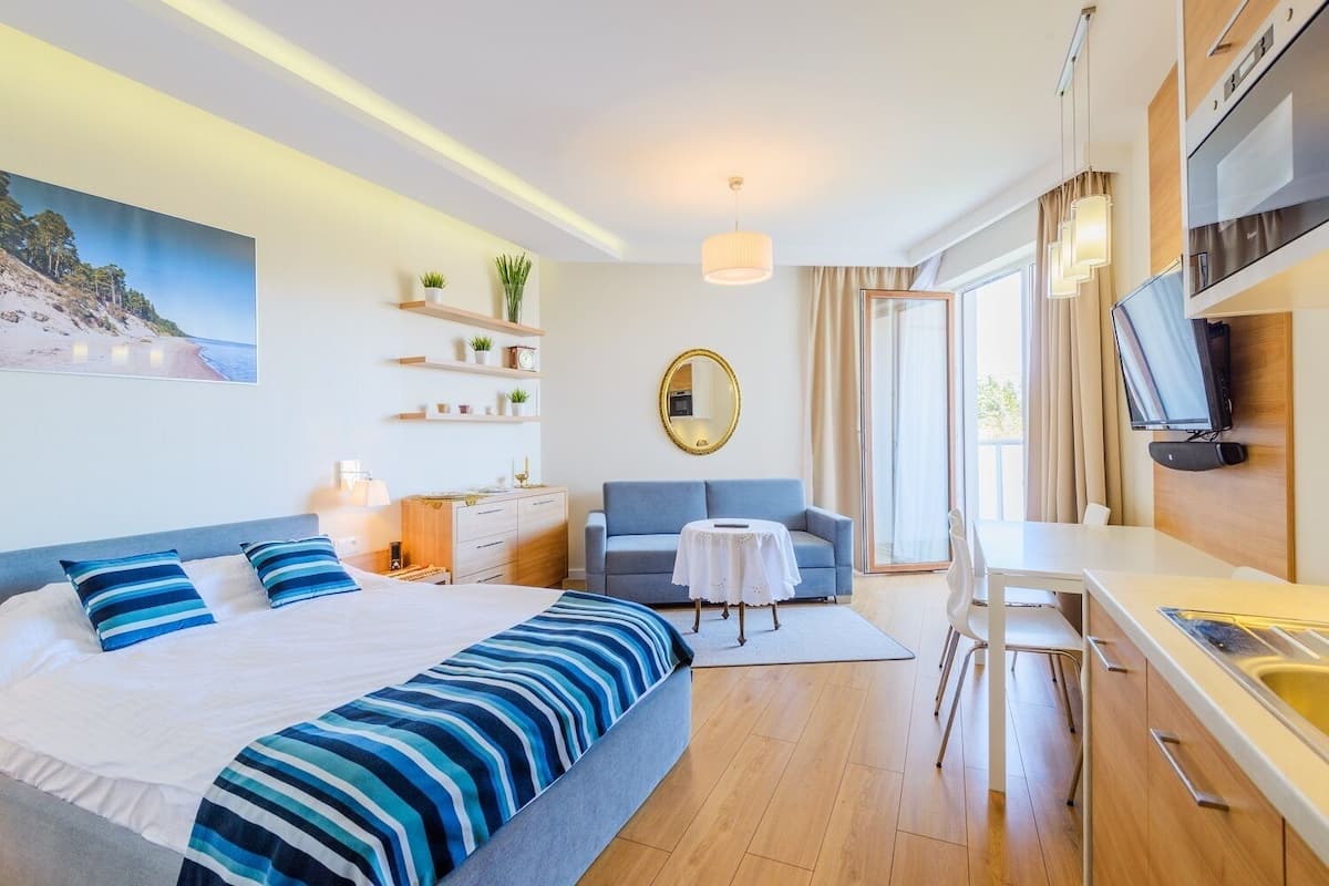 A modern hotel room with a bed, a desk, a chair, a small table, a TV, and a large window.
