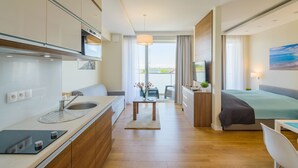 A modern hotel room with a kitchenette, a bed, a dining area, and a view of the outdoors. - Apartamenty NCNK Marina (Sztutowo)