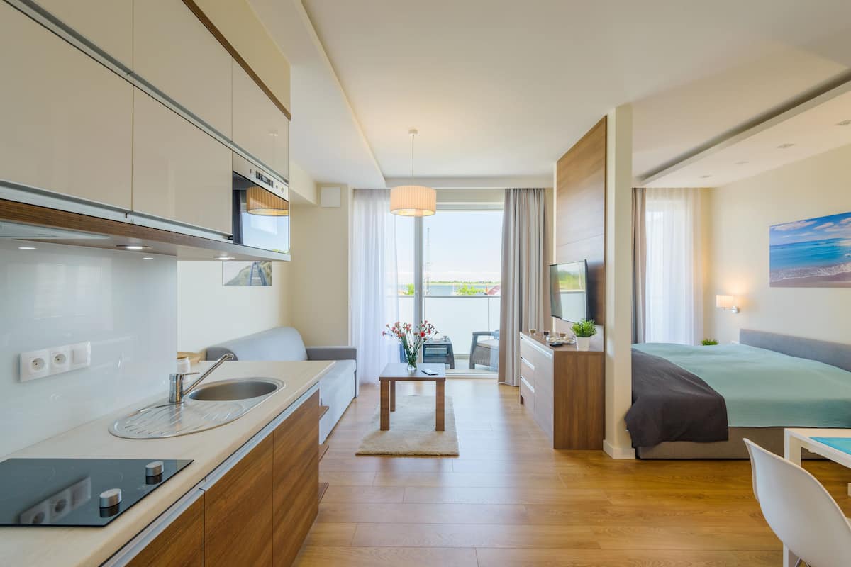A modern hotel room with a kitchenette, a bed, a dining area, and a view of the outdoors.