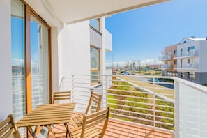 A balcony with a table and chairs, overlooking a parking area and buildings.
