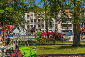 A residential building with multiple balconies, a grassy area with a swing set, and a tree.