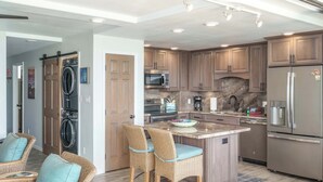 Eine moderne Küche mit Holzausbau, einer integrierten Mikrowelle, einem Kühlschrank und einer Kochinsel mit Sitzgelegenheiten.