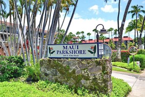 A sign for 'Maui Parkshore' with a stone base, surrounded by palm trees and greenery.