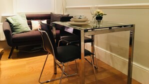 A dining area with a glass table, black chairs, a sofa with cushions, a floor lamp, and a vase with flowers. - 3 Bedroom Apartments Wells Street (London)