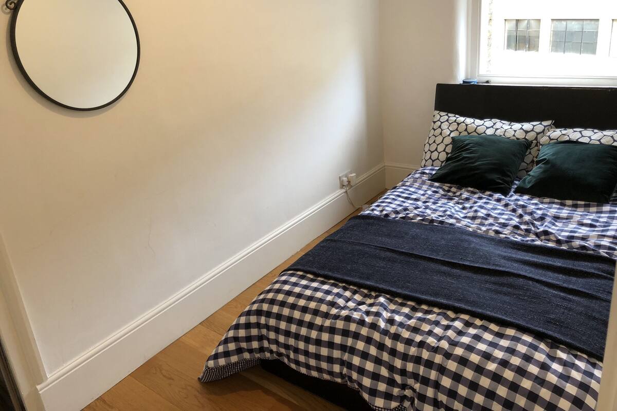 A bedroom with a bed, a round mirror, and a window.