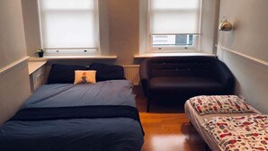 A small, compact bedroom with two single beds, a bench, and two windows with blinds. - 3 Bedroom Apartments Wells Street (London)