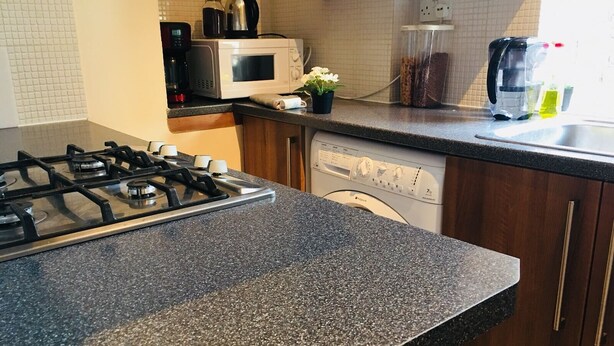 A kitchen with a gas stove, a microwave, a dishwasher, and wooden cabinets. - 3 Bedroom Apartments Wells Street (London)