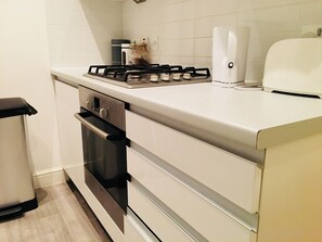 A kitchen with a gas stove, oven, and a trash bin. - 3 Bedroom Apartments Wells Street (London)