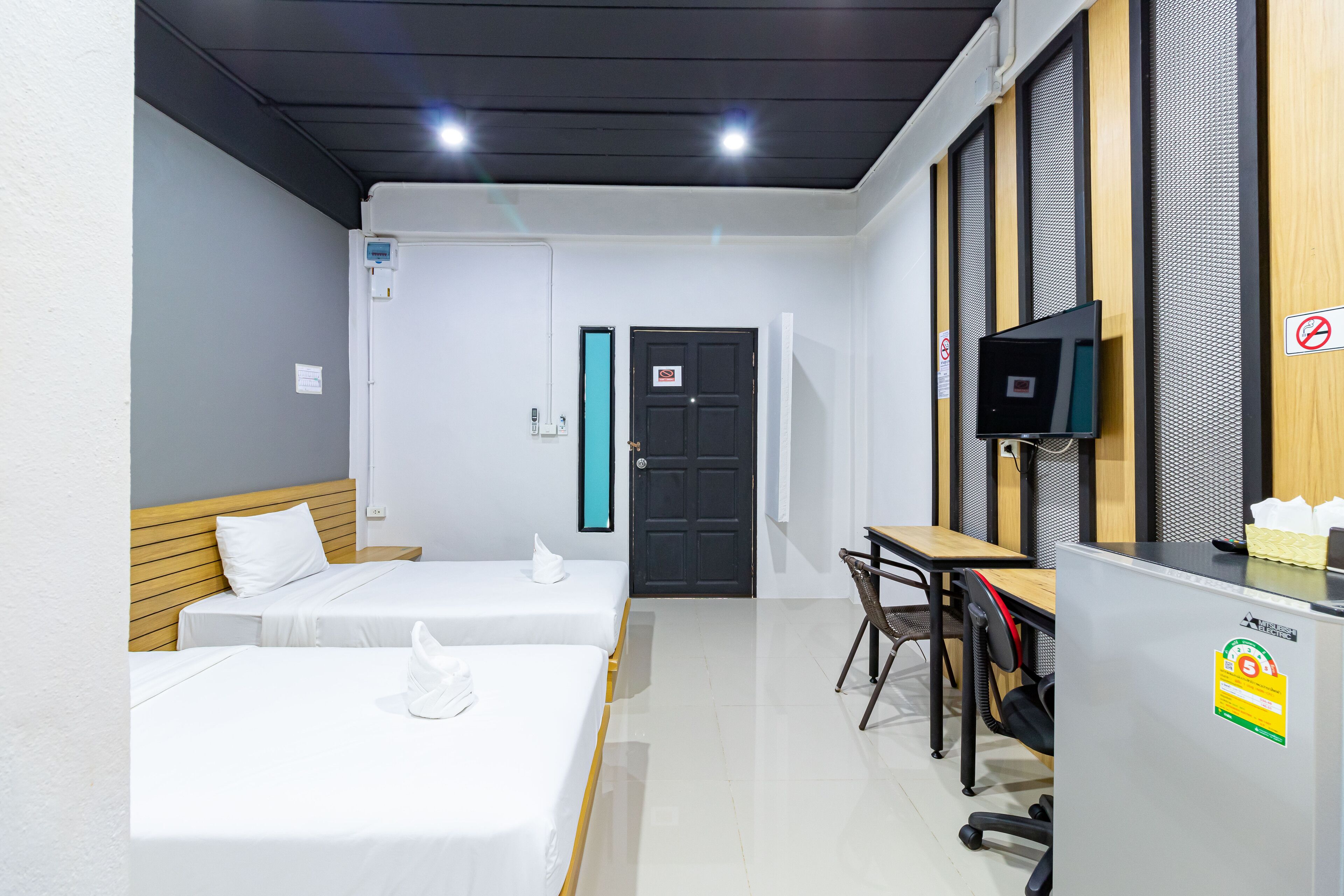 A hotel room with two beds, a desk, a chair, a TV, and a door with a sign.