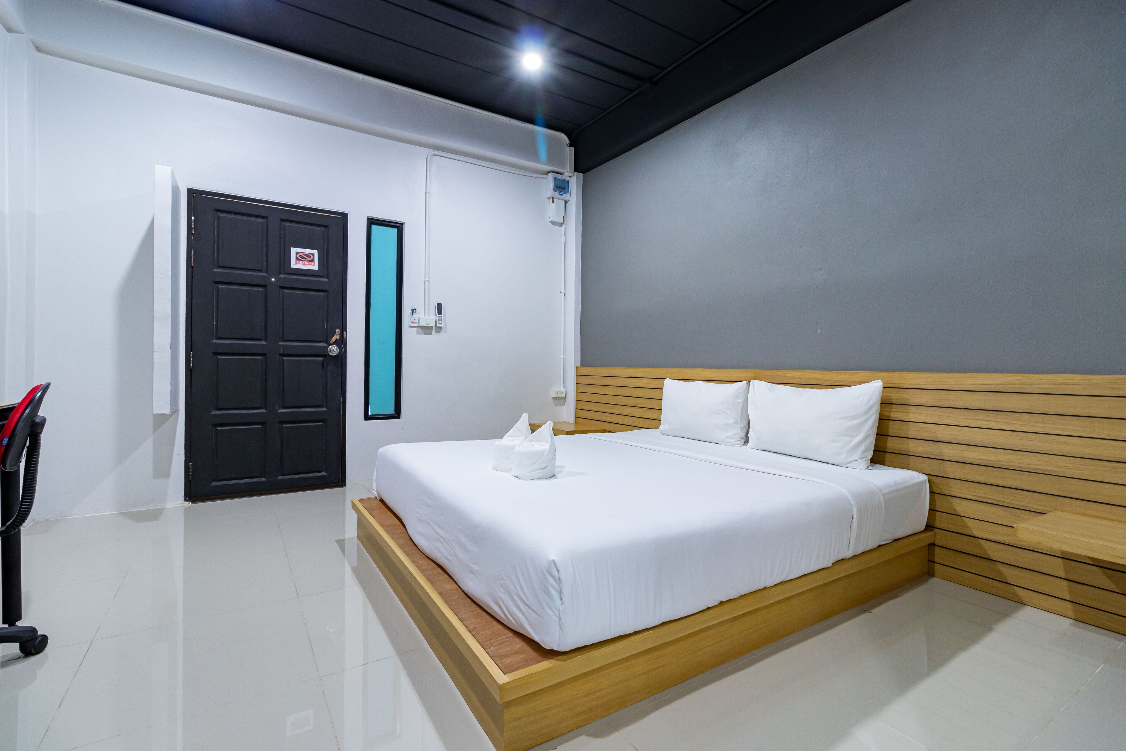 Una camera da letto moderna con un letto grande, una testiera in legno, una porta nera e un muro bianco.
