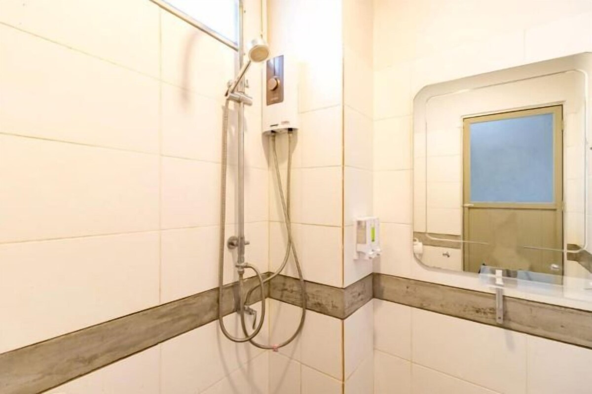 Ein Badezimmer mit weißen Fliesen, einer Dusche inklusive Duschbrause und einem Spiegel mit Fenster darüber.