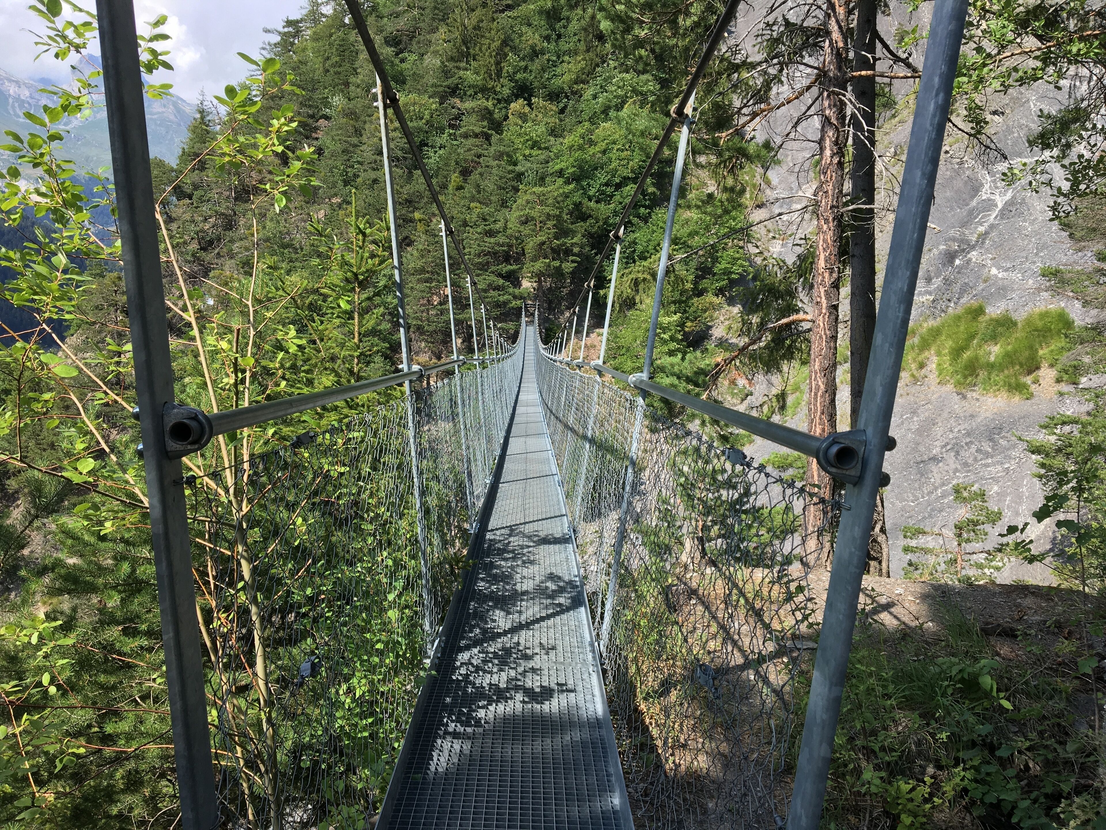 A suspension bridge surrounded by dense forest and rocky terrain.
